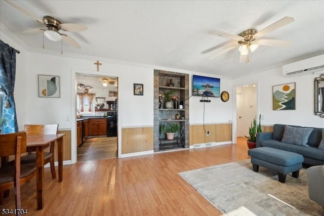 living room with wainscoting, ceiling fan, light wood finished floors, and a wall mounted air conditioner