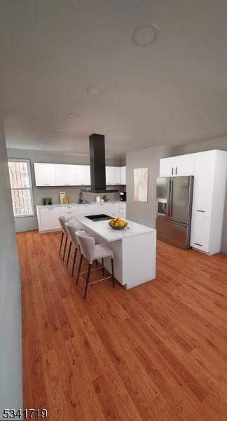 kitchen with light wood finished floors, light countertops, white cabinets, island range hood, and stainless steel fridge