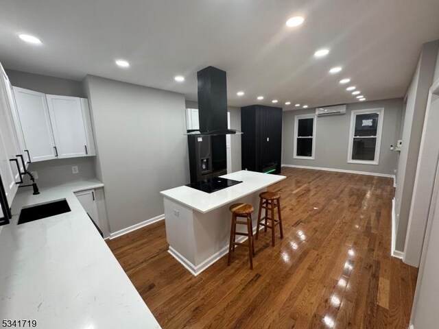 299 Halladay St, Jersey City, NJ 07304 - kitchen with island range hood, black electric cooktop, an AC wall unit, a breakfast bar area, and white cabinets