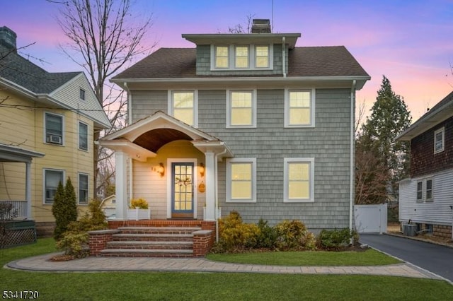 american foursquare style home featuring aphalt driveway, central AC, a chimney, and roof with shingles