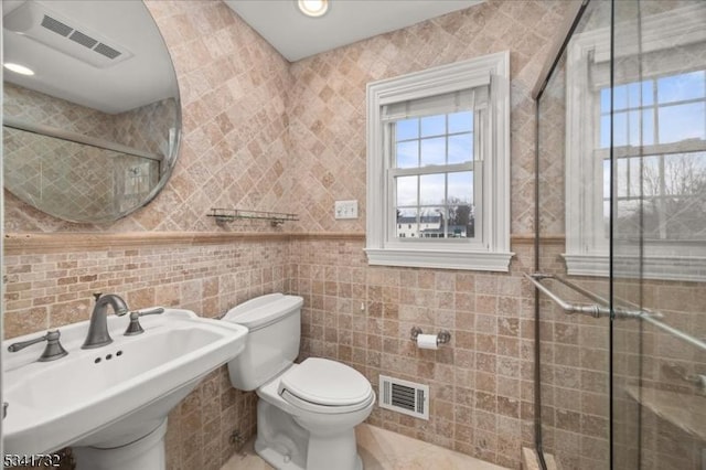 bathroom with a wealth of natural light, visible vents, and tile walls