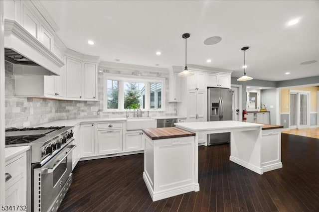 kitchen with stainless steel appliances, white cabinets, a sink, a kitchen island, and butcher block countertops