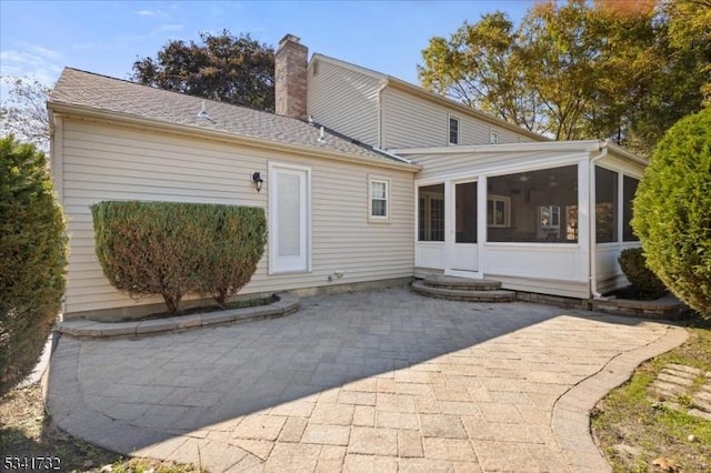 rear view of house with a sunroom, a chimney, and a patio