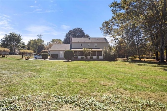 back of property featuring a garage, a lawn, and a sunroom