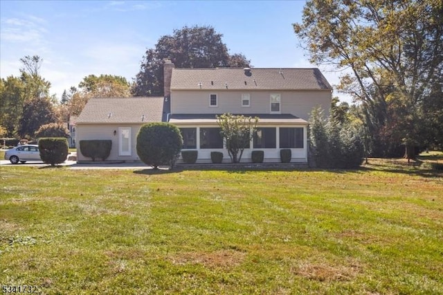 back of property featuring a sunroom, a lawn, and a chimney