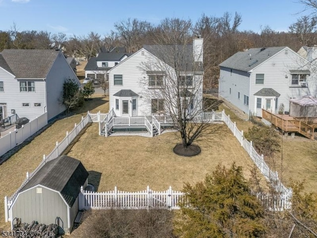 back of property with a fenced backyard, a chimney, a residential view, and a lawn