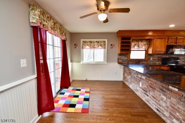 kitchen with wainscoting, dark countertops, brown cabinets, wood finished floors, and black appliances