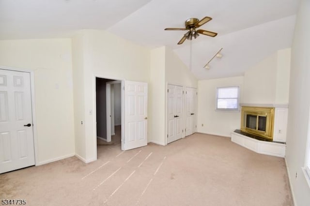 unfurnished living room with lofted ceiling, a glass covered fireplace, light carpet, ceiling fan, and baseboards