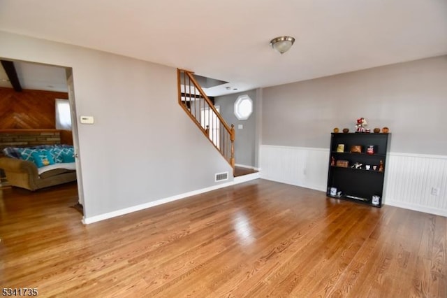 living area featuring a wainscoted wall, visible vents, stairway, and wood finished floors