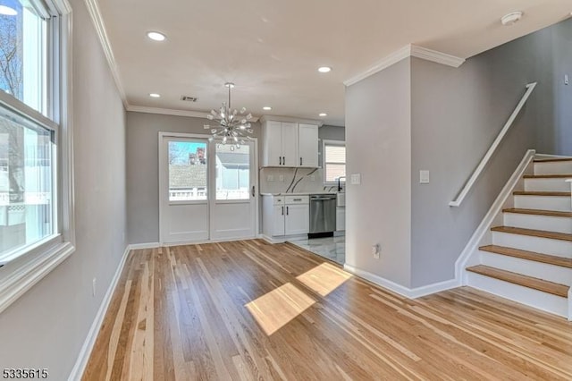 unfurnished dining area featuring ornamental molding, an inviting chandelier, light wood-style flooring, and baseboards