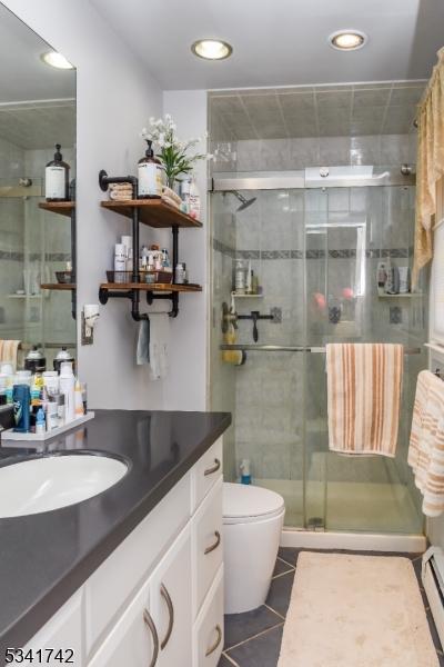 bathroom with a baseboard radiator, toilet, a stall shower, vanity, and tile patterned floors