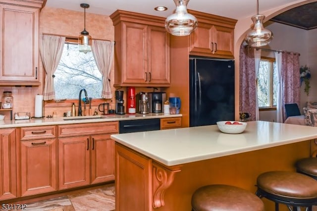 kitchen with arched walkways, brown cabinets, light countertops, black appliances, and a sink