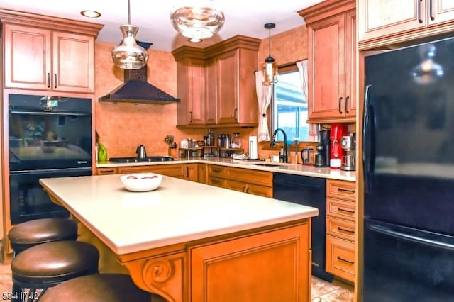 kitchen with pendant lighting, light countertops, a sink, wall chimney range hood, and black appliances