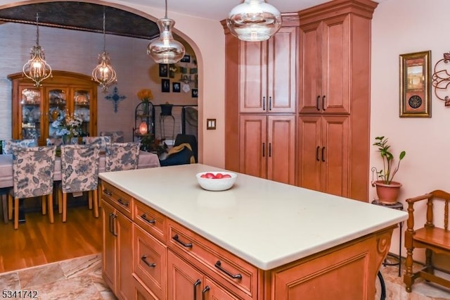 kitchen with arched walkways, light countertops, hanging light fixtures, and brown cabinetry