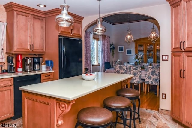 kitchen featuring a kitchen island, brown cabinets, a kitchen breakfast bar, light countertops, and black appliances