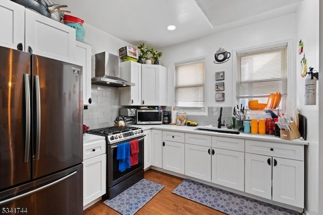 kitchen featuring a sink, light countertops, white cabinets, appliances with stainless steel finishes, and wall chimney exhaust hood