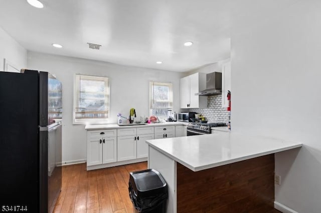 kitchen with wall chimney range hood, light countertops, a peninsula, stainless steel appliances, and a sink