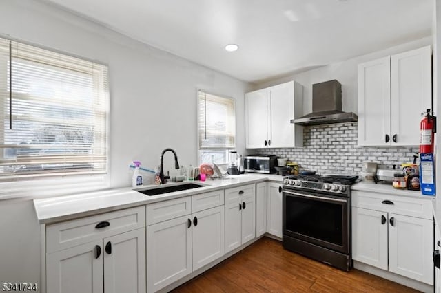 kitchen with a sink, white cabinets, stainless steel gas stove, wall chimney exhaust hood, and tasteful backsplash