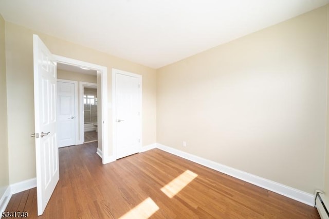 empty room featuring baseboards, baseboard heating, and wood finished floors