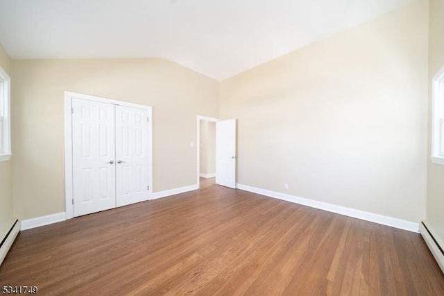 unfurnished bedroom featuring lofted ceiling, a baseboard radiator, baseboards, and wood finished floors