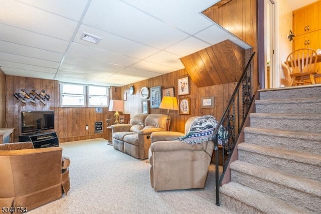 carpeted living area featuring visible vents, wood walls, stairway, and a drop ceiling