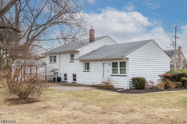 back of house featuring a shingled roof, a yard, a chimney, and central air condition unit