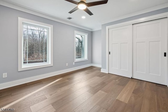 unfurnished bedroom with crown molding, a closet, visible vents, wood finished floors, and baseboards