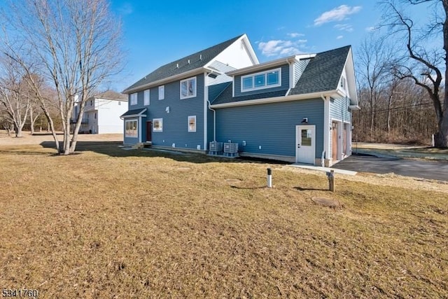 rear view of property with central air condition unit, driveway, a garage, and a yard