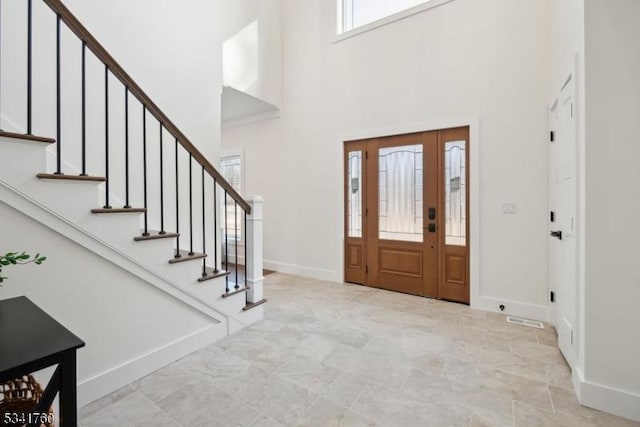 foyer featuring a towering ceiling, baseboards, visible vents, and stairway