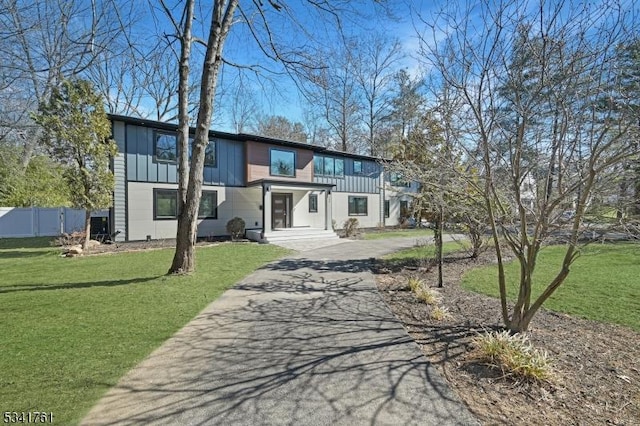 view of front of home featuring driveway, a front lawn, board and batten siding, and fence