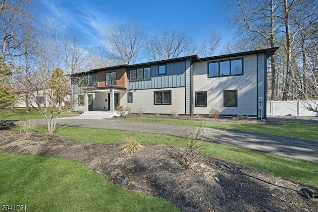 view of front facade featuring board and batten siding, a front yard, and fence