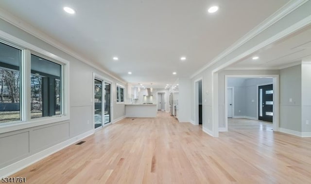 unfurnished living room with visible vents, light wood finished floors, a wealth of natural light, and crown molding