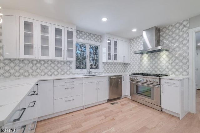 kitchen with wall chimney exhaust hood, appliances with stainless steel finishes, a sink, and white cabinetry