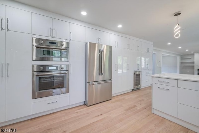 kitchen featuring light wood-style flooring, wine cooler, appliances with stainless steel finishes, hanging light fixtures, and white cabinetry