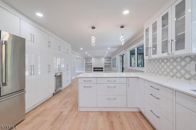 kitchen featuring wine cooler, a peninsula, white cabinets, high end fridge, and light wood finished floors