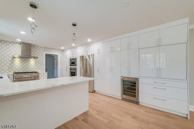 kitchen featuring high end appliances, light wood-style flooring, white cabinets, wall chimney range hood, and beverage cooler