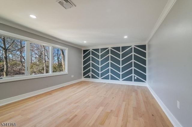 spare room with an accent wall, wood finished floors, visible vents, baseboards, and crown molding