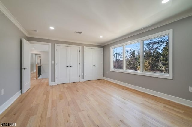 unfurnished bedroom with ornamental molding, visible vents, baseboards, and two closets