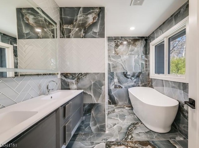 full bath featuring marble finish floor, a freestanding tub, and a sink