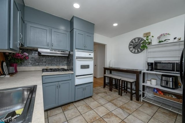 kitchen with stainless steel appliances, light countertops, under cabinet range hood, backsplash, and a warming drawer