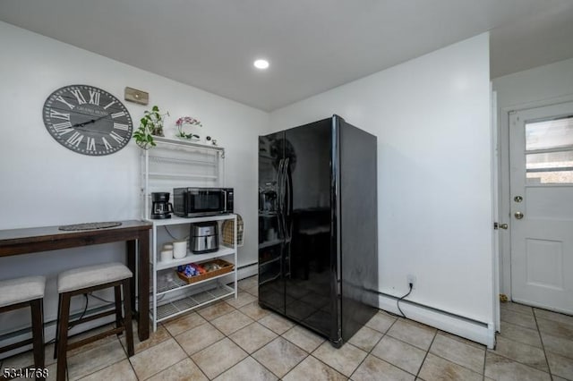 kitchen featuring light tile patterned floors, a baseboard radiator, stainless steel microwave, and black fridge