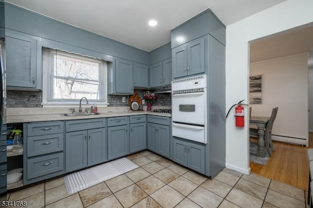 kitchen with oven, light countertops, a baseboard heating unit, a sink, and a warming drawer