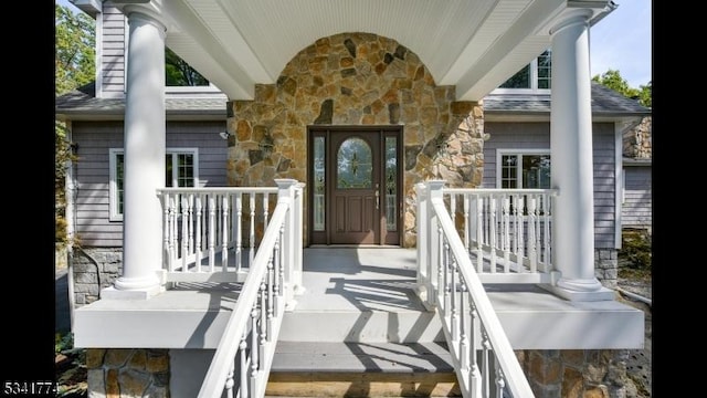 doorway to property with stone siding, covered porch, and a shingled roof