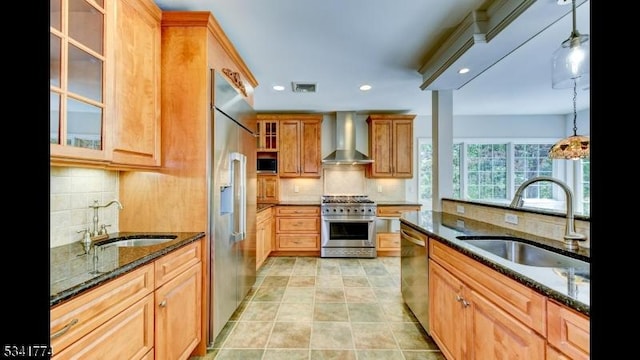 kitchen with a sink, high quality appliances, dark stone countertops, and wall chimney range hood