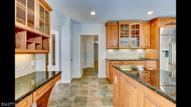 kitchen featuring dark stone counters, built in refrigerator, and tasteful backsplash