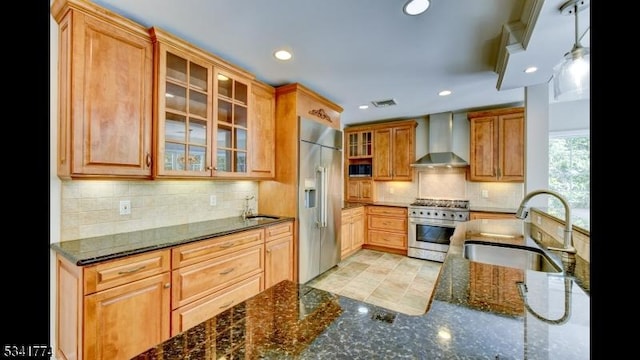 kitchen with visible vents, dark stone counters, premium appliances, wall chimney exhaust hood, and a sink