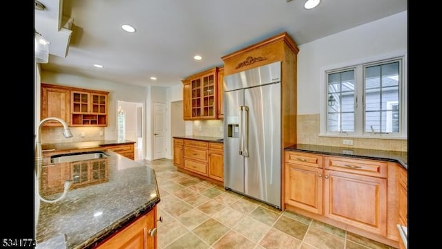 kitchen with stainless steel built in refrigerator, backsplash, glass insert cabinets, and a sink