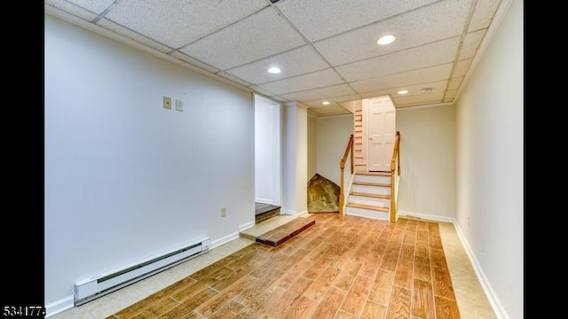 finished basement with baseboard heating, baseboards, stairs, and light wood-style floors