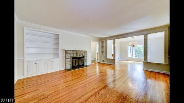 unfurnished living room featuring crown molding, a chandelier, built in features, light wood-type flooring, and a fireplace