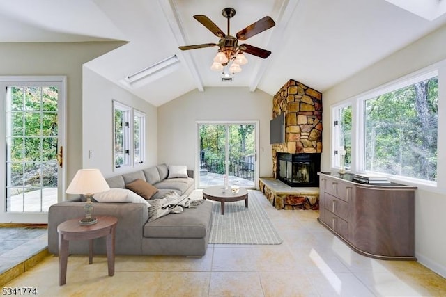 living room with lofted ceiling with skylight, a ceiling fan, a stone fireplace, light tile patterned flooring, and baseboards